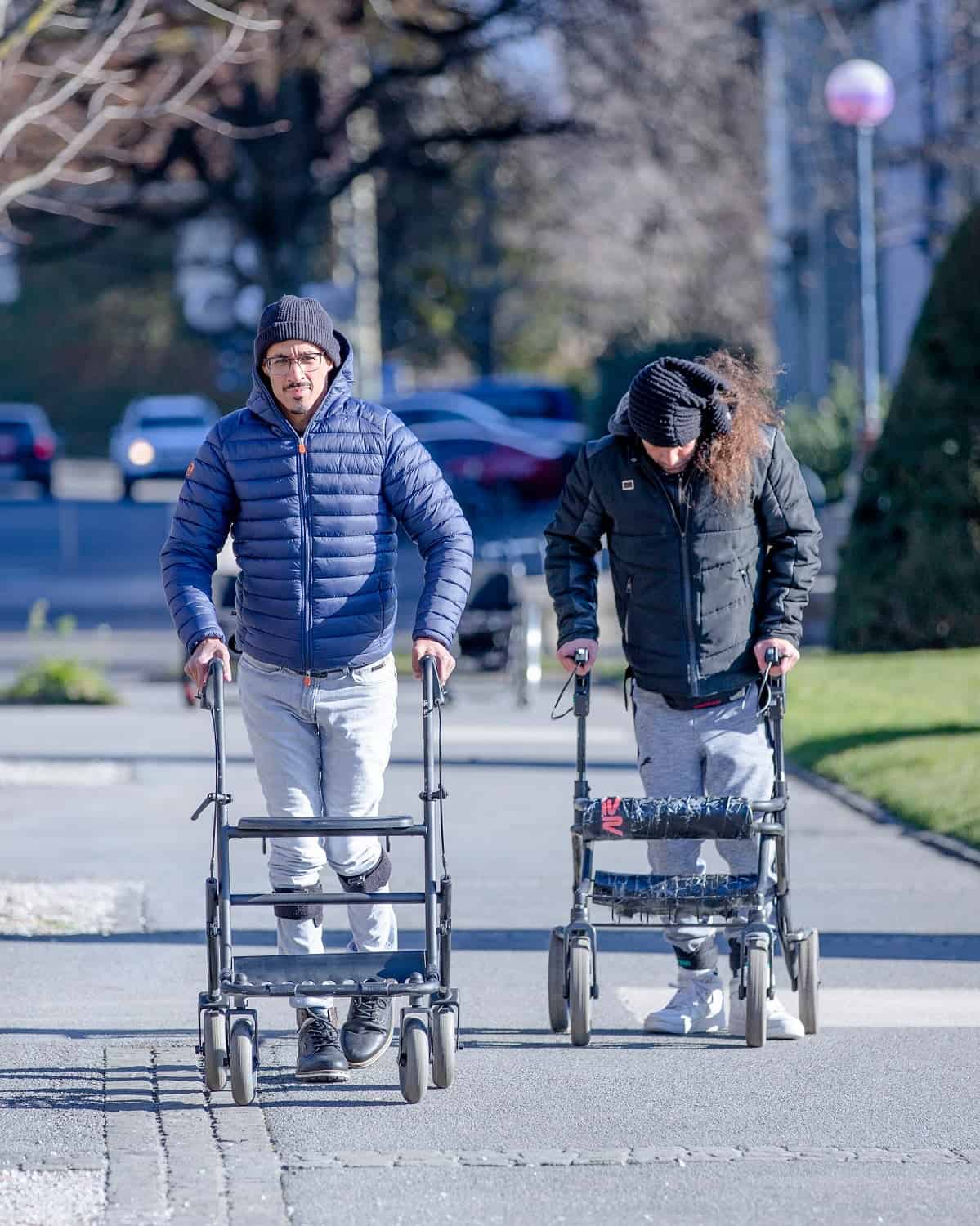 يمشي مريضان مصابان بالشلل على الرصيف بمساعدة جهاز للمشي بعد تلقي علاج التحفيز الكهربائي